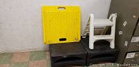 Yellow plastic ramp on top of two black step stools, next to white two-step stool