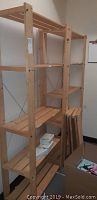 Three wooden shelving units, plank style, with metal cross braces for support. Light natural wood color, standing in room with some items on lower shelves.