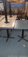 Photo showing side-by-side view of two tables with light beige and dark gray tops, metal pedestal bases, worn surfaces with marks and scratches.