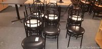Photo of eleven black metal chairs with rounded backs and round seats, some chairs showing wear and damage on seat cushions.