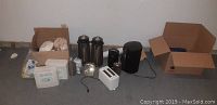 Overview of all items included in the lot on the floor, showing coffee maker, two carafes, toaster, kettle, and boxes of coffee supplies.