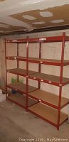 Front view of three tall metal shelving units made of red metal frames and particle board shelves against a basement wall