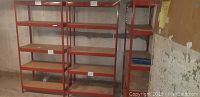Three red metal shelving units arranged side by side against concrete wall
