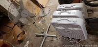 Four white square box fans arranged on floor with one adjustable stand fan in the background, showing overall lot contents
