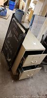 Photo showing metal filing cabinet with two drawers open and black sandwich board sign with chalk writing placed next to it in basement setting