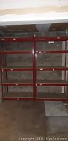 Front view of two red metal shelving units with multiple wooden shelves in a basement with concrete wall and floor.
