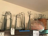 Photo of multiple metal doll stands of various shapes and sizes lined up against a wall beside a woven basket filled with soft packing materials.