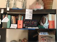 Shelf showing craft books, doll patterns, and scrapbooks in multiple colored magazine holders and binders with other craft items.
