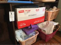 View of a Staples copy paper box on top of baskets containing folded fabric and trims, small stuffed animals visible in the back basket.