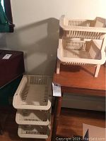 Set of three beige plastic detachable storage baskets stacked vertically on a frame.