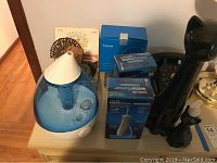 Wide view of all lot items showing vaporizer, boxes of Waterpik water flossers, ceramic black cat, soap dispenser, rotary phone, and boxed bathroom items.