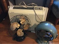 Panasonic window air conditioner unit with two vintage fans placed in front on the floor.