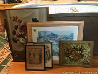 Seven pieces of wall art grouped together showing various frame styles and subject matter including floral paintings and vintage prints.