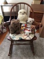 Front view of the wooden rocking chair with 8 assorted stuffed animals placed on the floral cushion on the seat.