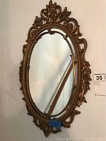 Full view of the ornate oval hanging mirror with gold frame and baroque style detailing.