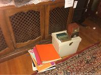 Various binders and folders with sheet music on floor beside wooden cabinet