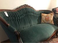 Full view of vintage settee couch showing green tufted velvet upholstery, carved wood frame, and pillow (not included).