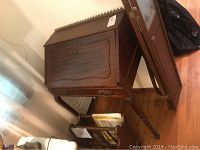 Front and side view of vintage wooden writing desk with foldable slant top and magazine rack beneath it, showing desk's curved legs and decorative edge detail.