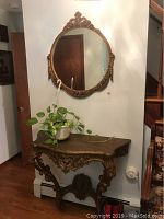 Round wall mirror with carved gilt wooden frame, shows repaired crack, hanging on wall above entryway table.
