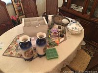 Wide shot showing vases, silver plated trays, stemware glasses, and covered dish on dining table.