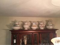 Full view of five ceramic jugs with bowls displayed on top of a wooden cabinet.