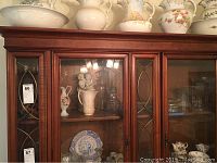 Glassware, cut glass bowls, and vases displayed on a wooden glass-front cabinet top shelf and inside