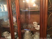 Cabinet containing assorted cut glass bowls, crystal candlestick, china plates and teacups arranged together.