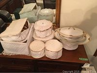 Photo of the entire china set packed and arranged on a wooden dresser including various padded quilted protective cases and the plates and serving dishes.