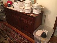 Wood buffet shown with storage containers and ceramics on top, positioned near a rug and wall.