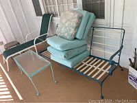 Wrought iron patio sofa with cushions and glass-top table on porch.