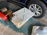 Photo of off-white plastic cat carrier with ventilation slots and door, topped by multiple gray fabric pads with textured surfaces and handles.