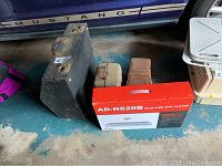 Photo showing all items including black accordion case, DVD player box, camera cases, and projector case on garage floor.