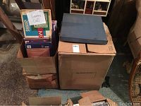 Three cardboard boxes filled with assorted vintage board games stored indoors.