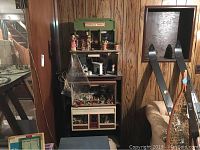 Overall view of multiple doll house sets stacked together with miniature figures and furniture displayed inside a multi-level shelving unit.