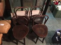 Overall view of four bentwood wooden chairs placed together in a dimly lit room, showing their curved backs and dark wooden seats.