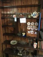 Photo showing wood shelves with multiple glassware including clear textured glasses, bowls, and pitchers alongside a blue floral porcelain tea set with cups and plates.