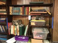 Shelf containing hardcover children's books and boxes stacked, some boxes contain doll furniture and mini electric lamps.