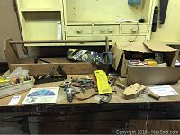 General view of the workbench with various hand tools laid out including hand planes, clamp, saw, drill, and boxes containing blades and nails.