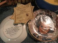 Close-up photo showing backstamp of a Knowles ceramic plate and certificate of authenticity for French dolls.