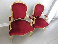 Pair of matching red corduroy upholstered armchairs with gold painted wood frames, front view showing seat and back upholstery.