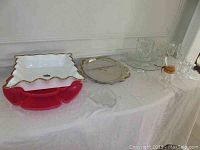 Full view of all items on white covered table including red plastic trays, porcelain dish, stainless platter, glassware and carafe