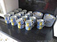 Full set of 30 cups and 31 saucers displayed on counter showing design and condition