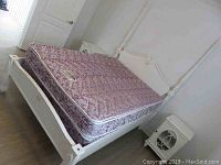 Front angle view of white painted wooden double poster bed with pink floral mattress and box spring.