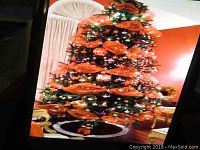 Front view of the full decorated artificial Christmas tree with orange ribbons and multi-colored lights.