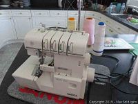 Full view of Omega serger machine on protective pad with thread spools and foot pedal attached.