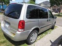 Rear and passenger-side view of silver Uplander showing rust on bumper and dents on rear quarter panel