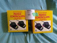 Four Atari CX30 paddle controllers in original yellow boxes displayed on blue fabric surface.