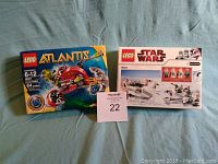 Photo of sealed Lego Atlantis 8057 and Lego Star Wars 8084 sets on blue fabric background, with MaxSold auction tag