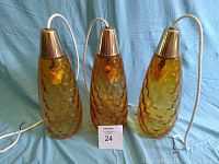Three amber glass pendant lights with honeycomb texture alongside white cords and chrome tops shown against a blue cloth background.
