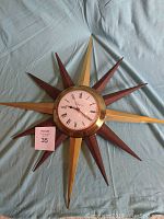 Full view of vintage Ingraham starburst atomic wall clock on cloth background. Shows complete starburst design alternating brass and wood rays with clock face at center.
